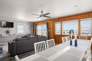 Una sala de estar con sofá, mesa de comedor, sillas, ventilador de techo y televisor.