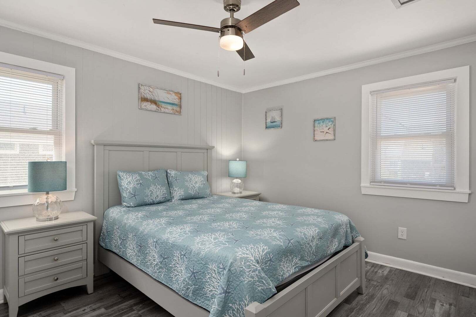 A bedroom with a bed, a nightstand, a lamp, a ceiling fan, and artwork on the walls.
