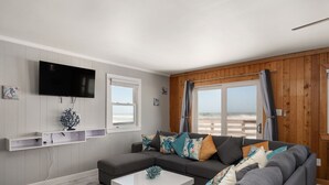 A modern living room with a grey sofa, a white coffee table, and a flat-screen TV mounted on the wall. - 600 Nags Head Ocean-Front Completely Renovated (Nags Head)