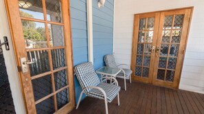 A covered patio area with two chairs and a table, wooden doors with glass panels, and a blue exterior wall. - Picnic Cottage, Lovely home near the beach (PICNIC BAY)