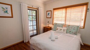 Ein Schlafzimmer mit Bett, Nachttisch, Fenster mit Jalousien und Tür mit Vorhang.