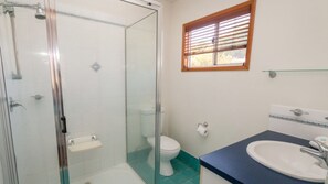 A bathroom with a glass-enclosed shower, a toilet, and a sink with a blue countertop. - Picnic Cottage, Lovely home near the beach (PICNIC BAY)