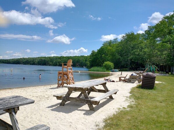 A lakeside picnic area with wooden benches and a lifeguard chair.