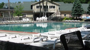 Una piscina con sillones blancos y un edificio con balcón al fondo.