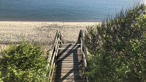 Ein hölzerner Steg führt zu einem Sandstrand mit einem Boot im Wasser.