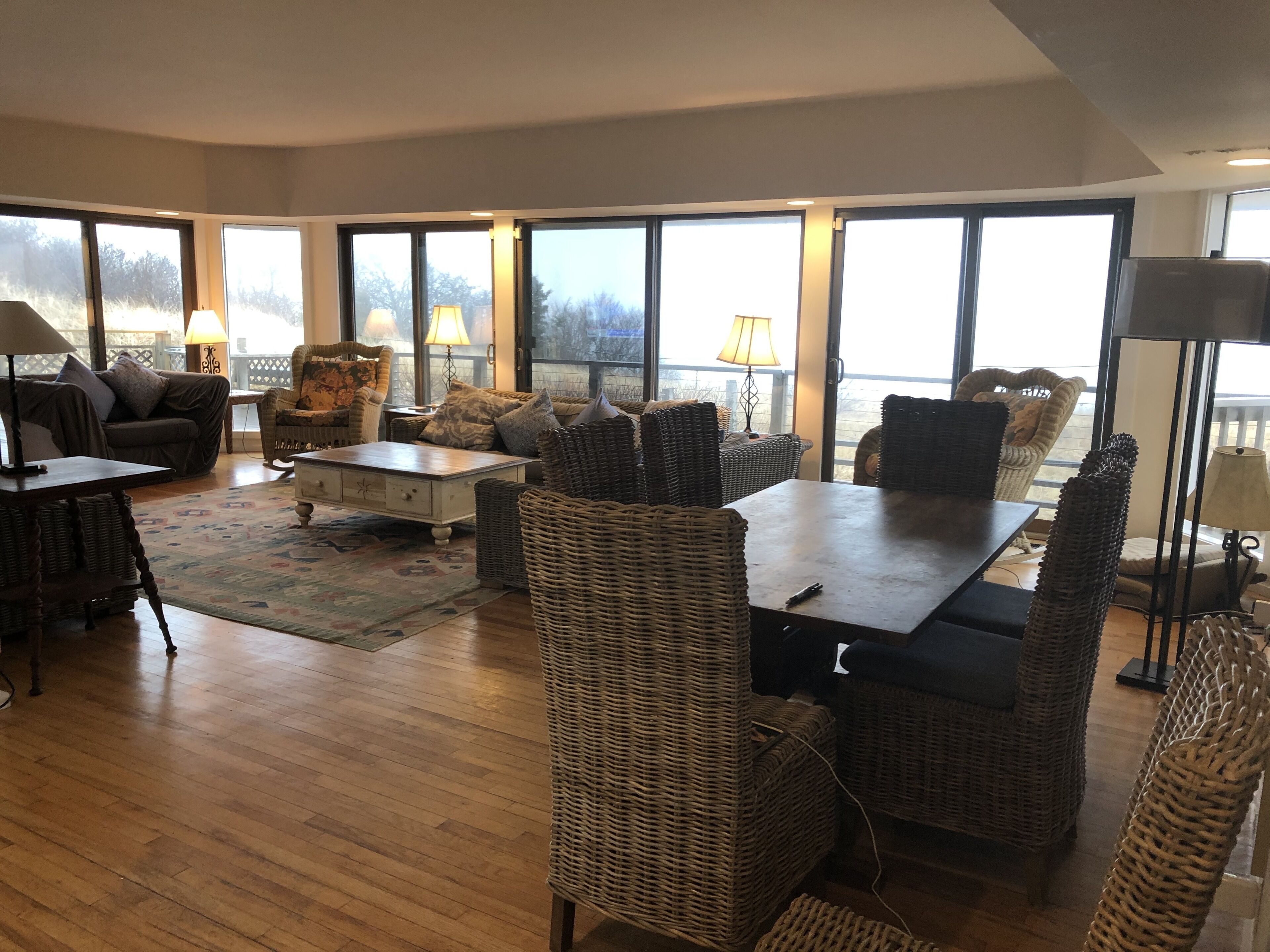 Amplia sala de estar con un ventanal grande, muebles de mimbre y piso de madera.
