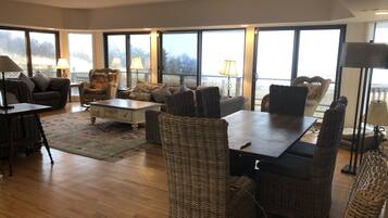 Amplia sala de estar con un ventanal grande, muebles de mimbre y piso de madera.