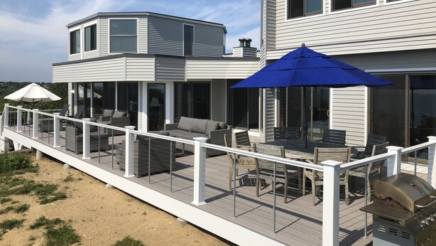 Ein modernes, zweistöckiges Haus mit einer überdachten Terrasse, die Gartenmöbel und einen Grill bietet.