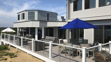 Una casa moderna de dos pisos con un patio cubierto que cuenta con mobiliario exterior y una parrilla.