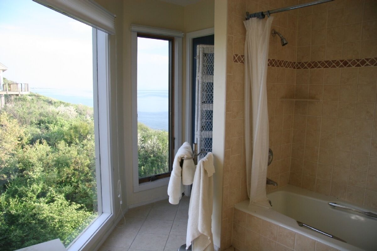 A bathroom with a bathtub, a shower curtain, and a window offering a view of greenery and a building.