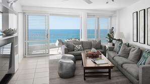 A modern living room with a view of the ocean, a ceiling fan, and a large window with blinds.