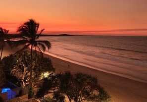 Une plage au coucher du soleil, avec des palmiers et un espace piscine.