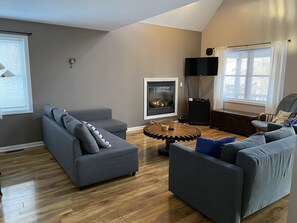 A modern living room with a fireplace, grey sofas, and a wooden coffee table. - Angel Baby Lodge Winnipesauke dog/family friendly contemporary home (Moultonborough)