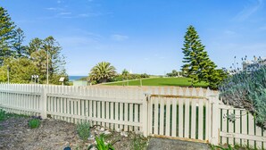 A fenced garden with a grassy area, trees, and a view of the sea. - Perfect Position in Port Elliot Wifi (Port Elliot)