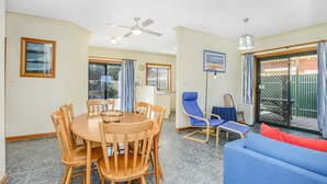 A dining area with a round wooden table and chairs, a ceiling fan, and a view of the outside through a glass door. - Perfect Position in Port Elliot Wifi (Port Elliot)