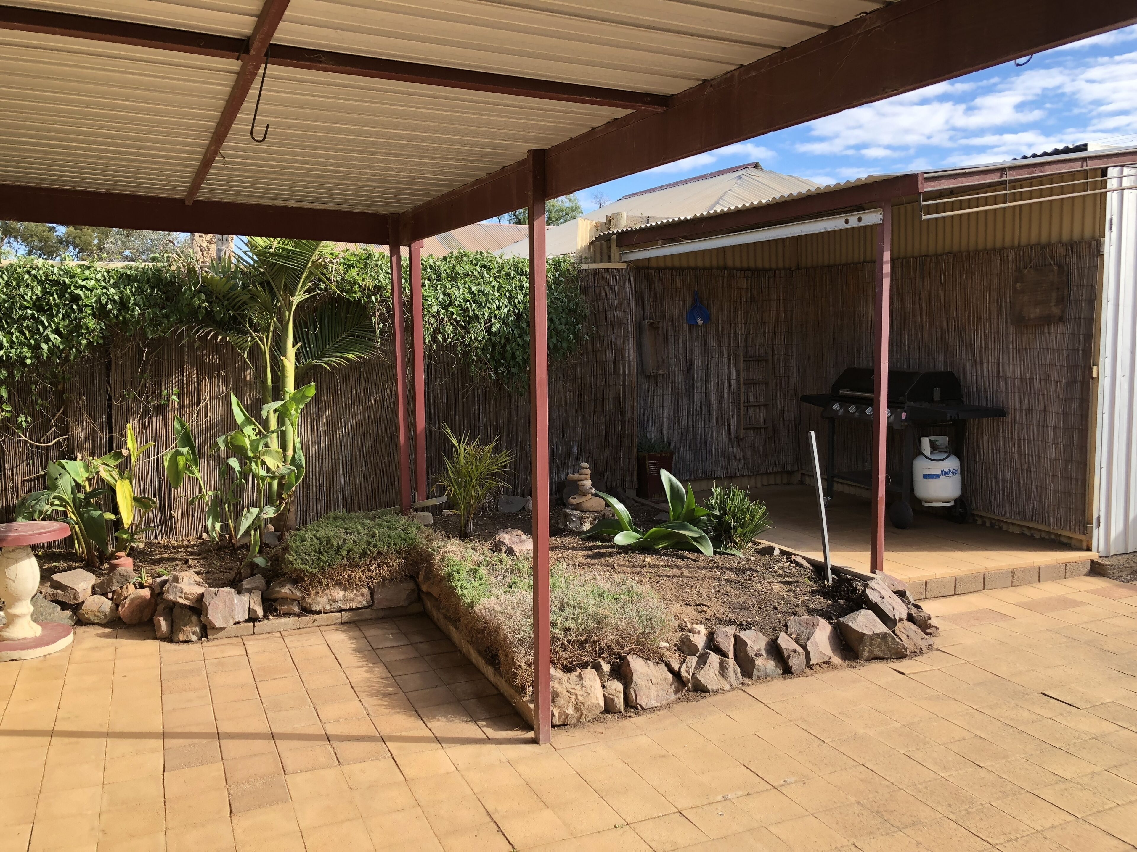 A covered patio area with a tiled floor, a bamboo fence, and various plants.