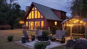 A log cabin with a large deck, outdoor seating, and a covered area with string lights.