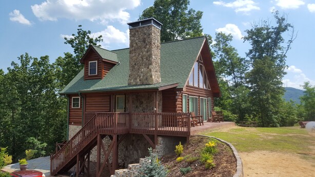 A log cabin with a stone chimney, a wooden deck, and a stone staircase leading to the entrance.