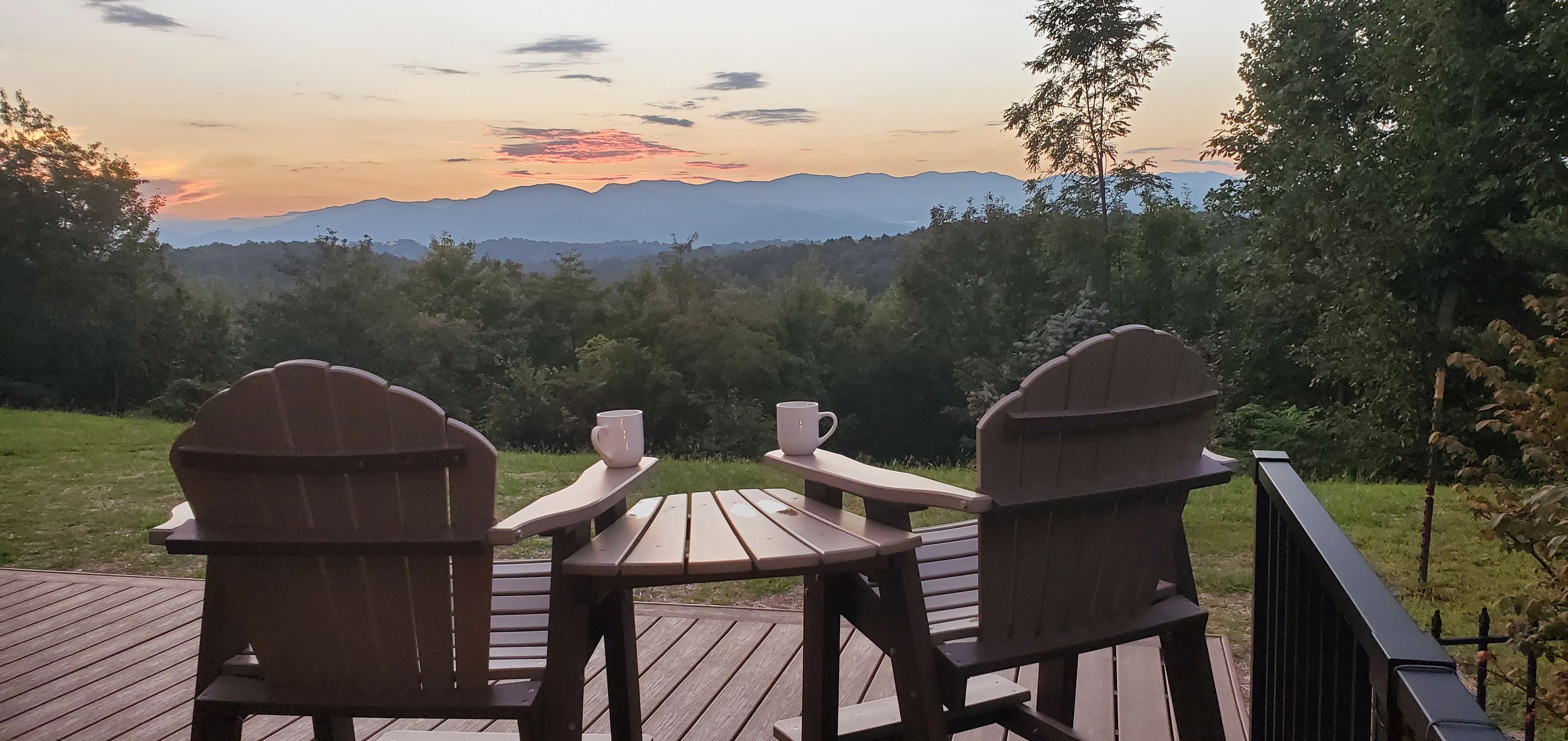 A wooden deck with Adirondack chairs and a table, overlooking a mountainous landscape.
