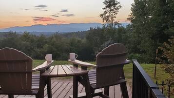 A wooden deck with Adirondack chairs and a table, overlooking a mountainous landscape.