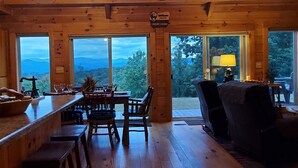 A spacious wooden cabin interior with a high ceiling, large windows, a dining area, and a bar.