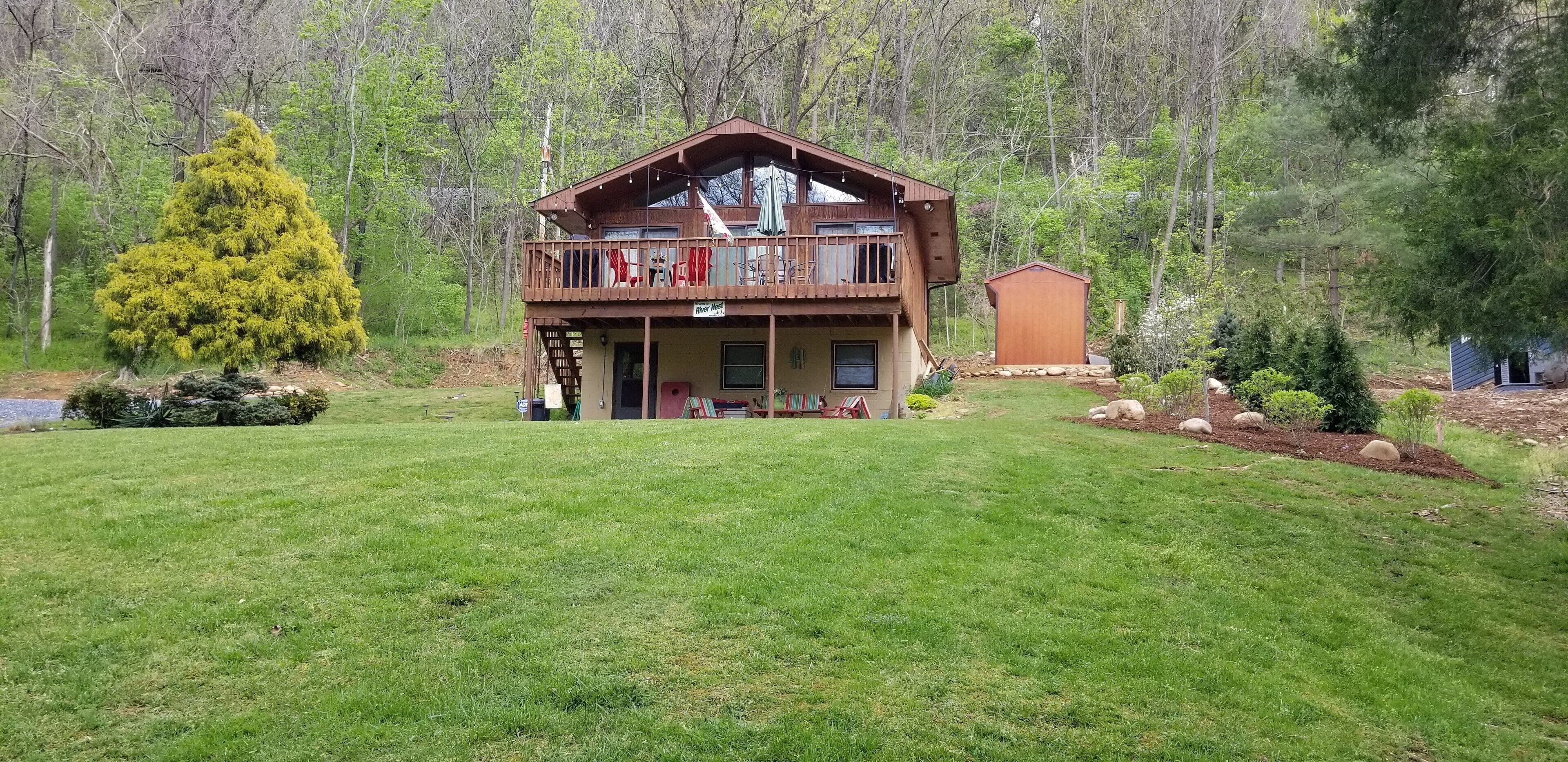 Une cabane à deux étages dotée d’un balcon, entourée d’une pelouse bien entretenue et d’arbres.