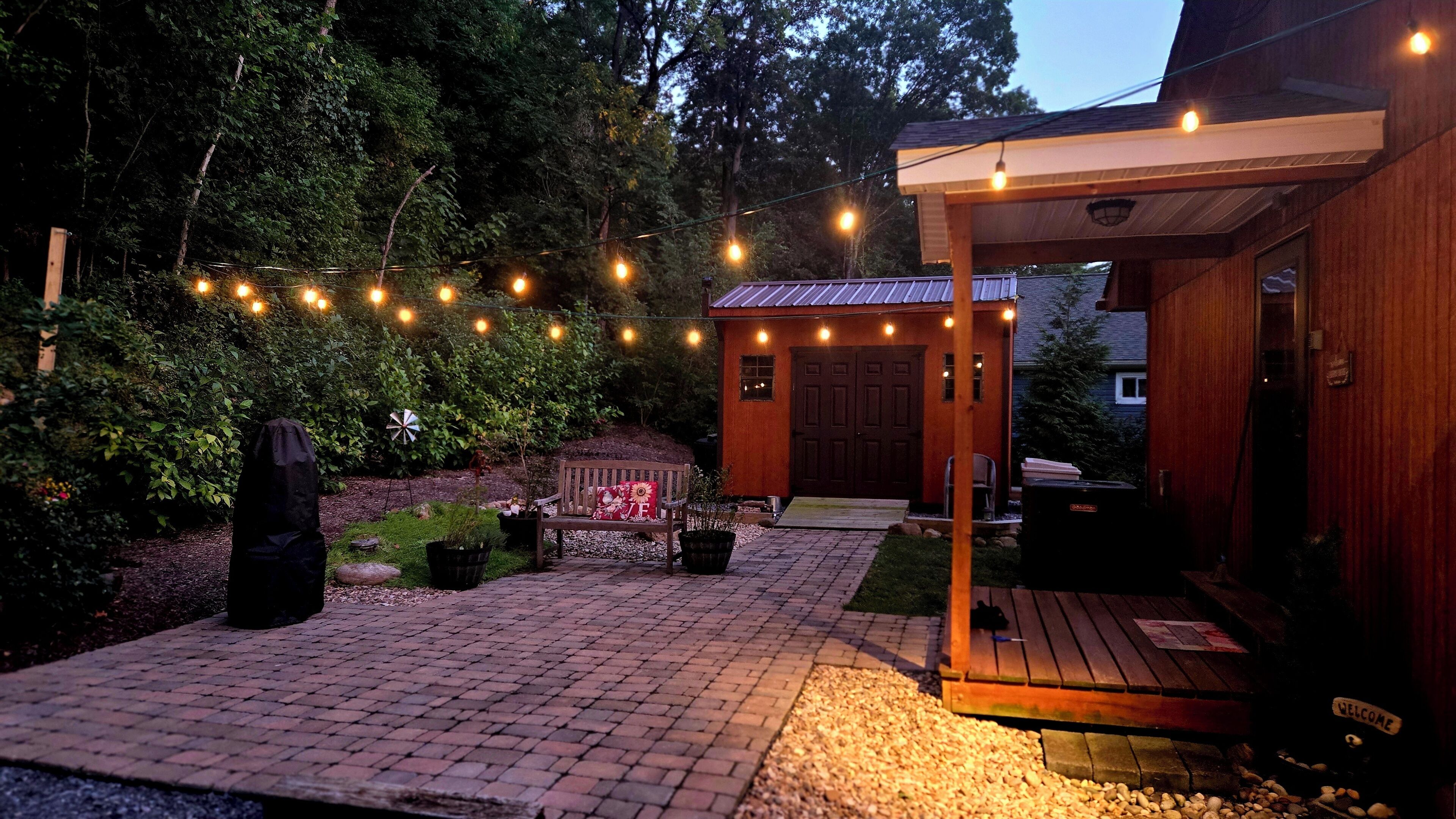 A wooden cabin with a porch, string lights, and a bench.