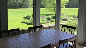 A dining area with a large table and chairs, large windows offering a view of a green landscape.