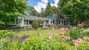 A two-story house with a stone retaining wall and a well-maintained garden with various flowers and shrubs.
