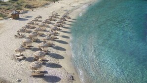 Vista aerea di una spiaggia con file di lettini e ombrelloni, una piccola capanna e acqua cristallina color turchese.