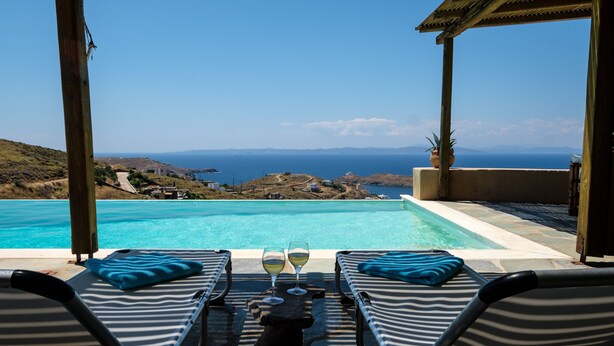 Zona piscina con sedie a sdraio e un tavolo con bicchieri, con vista sul paesaggio costiero.