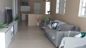 Een moderne woonkamer met een grijze bank, een televisie op een meubel en een keuken in de achtergrond.