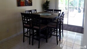 A dining area with a round table and chairs, a chandelier, a painting on the wall, and a sliding glass door leading to a balcony. - 5 Min Walk to Beach, Heated pool w/ spa jets, Large private lanai facing SW. (Marco Island)