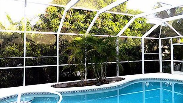A swimming pool with a glass enclosure, surrounded by lush greenery. - 5 Min Walk to Beach, Heated pool w/ spa jets, Large private lanai facing SW. (Marco Island)