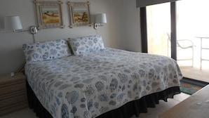 A bedroom with a bed, two wall-mounted lamps, and two framed paintings. - Oceanfront - Beautiful, Direct Oceanfront. Extra Large 1 Bedroom, 1+ Bath (New Smyrna Beach)