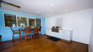 A modern kitchen with wooden flooring, white cabinets, and a built-in grill. - A beach house with colour! (Shoal Bay)