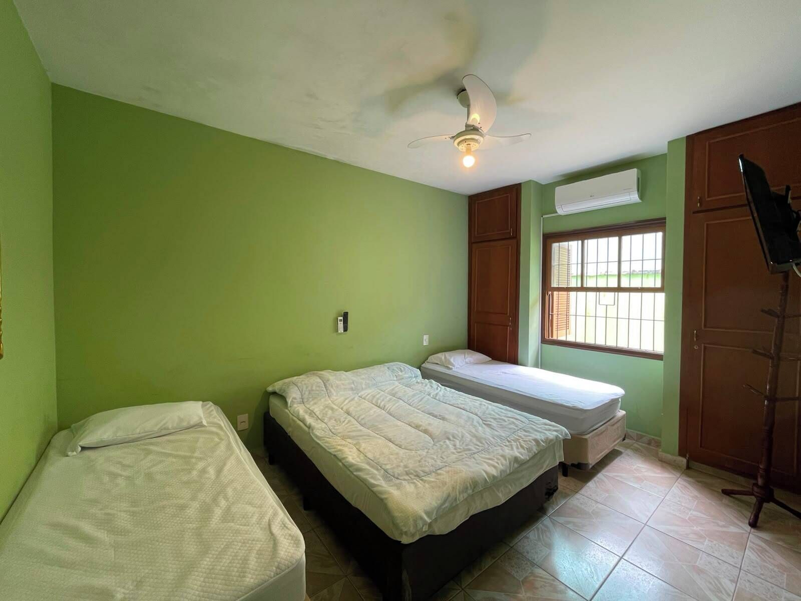 A room with two beds, a ceiling fan, a window with bars, and a door.