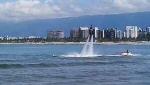 Eine Uferstadt mit Springbrunnen, einem Jetski und einem fernen Gebirge.