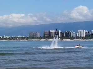 A waterfront cityscape with a fountain, a jet ski, and a distant mountain range. - House with air conditioning 50m from Riviera Beach, house with Wi-Fi.  (Bertioga)