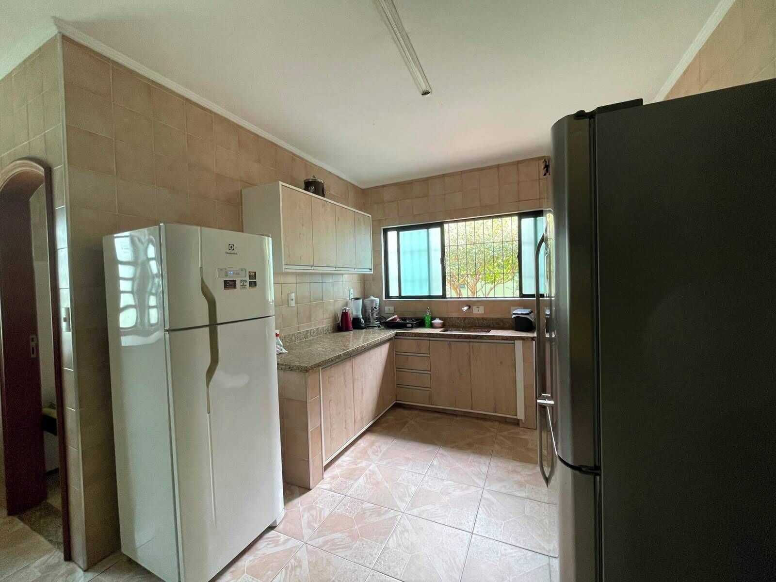 Una cocina con refrigerador, pileta, alacenas y ventana.