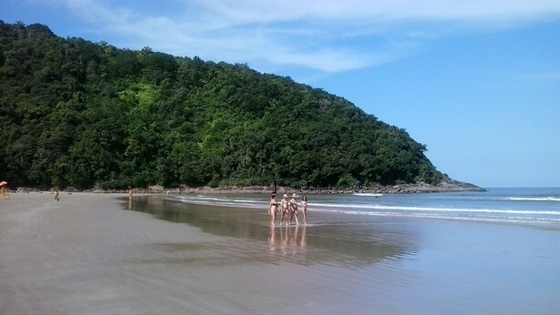 Ein Strand mit einer bewaldeten Hügelkette im Hintergrund.