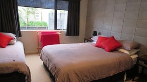 Ein Hotelzimmer mit zwei Betten, einem Fenster mit Vorhängen, einem Nachttisch mit Lampe und Blick auf Grünfläche.
