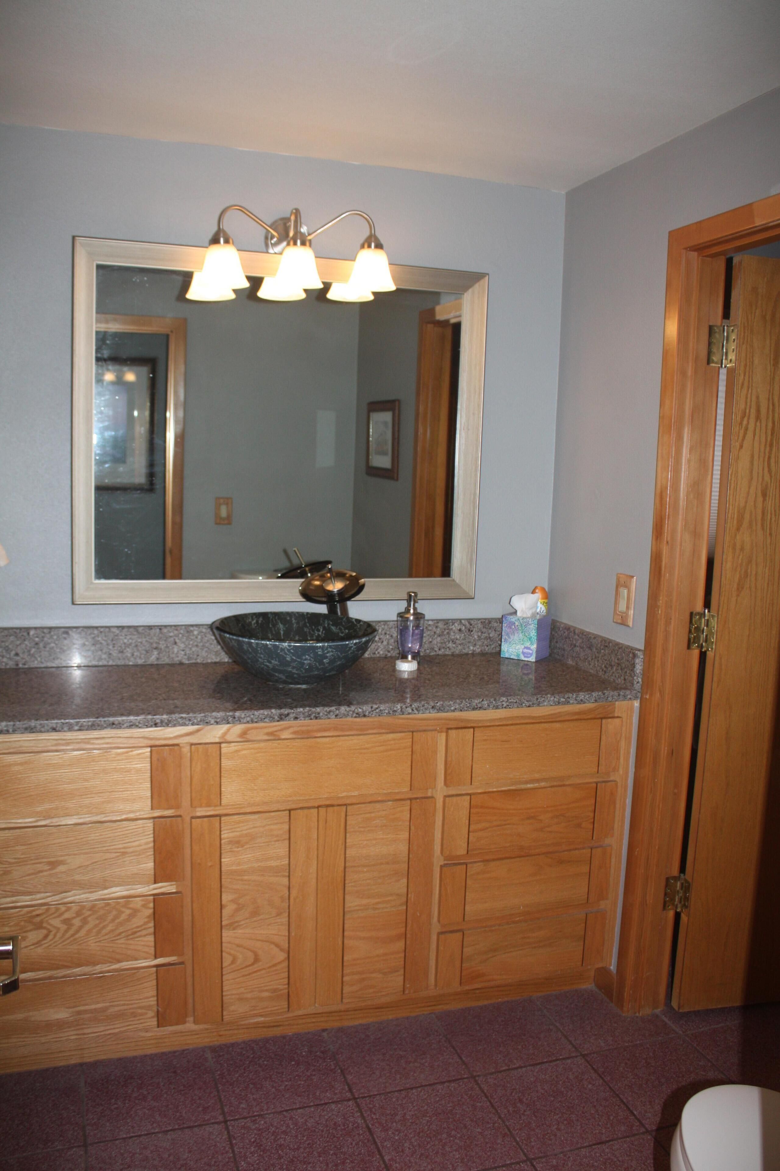 Une salle de bain avec un meuble-lavabo en bois, un grand miroir et un lavabo en forme de cuvette.