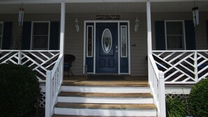 Une maison à deux étages avec une porte d’entrée bleue, des balustrades blanches et une pancarte « Bienvenue » au-dessus de la porte.