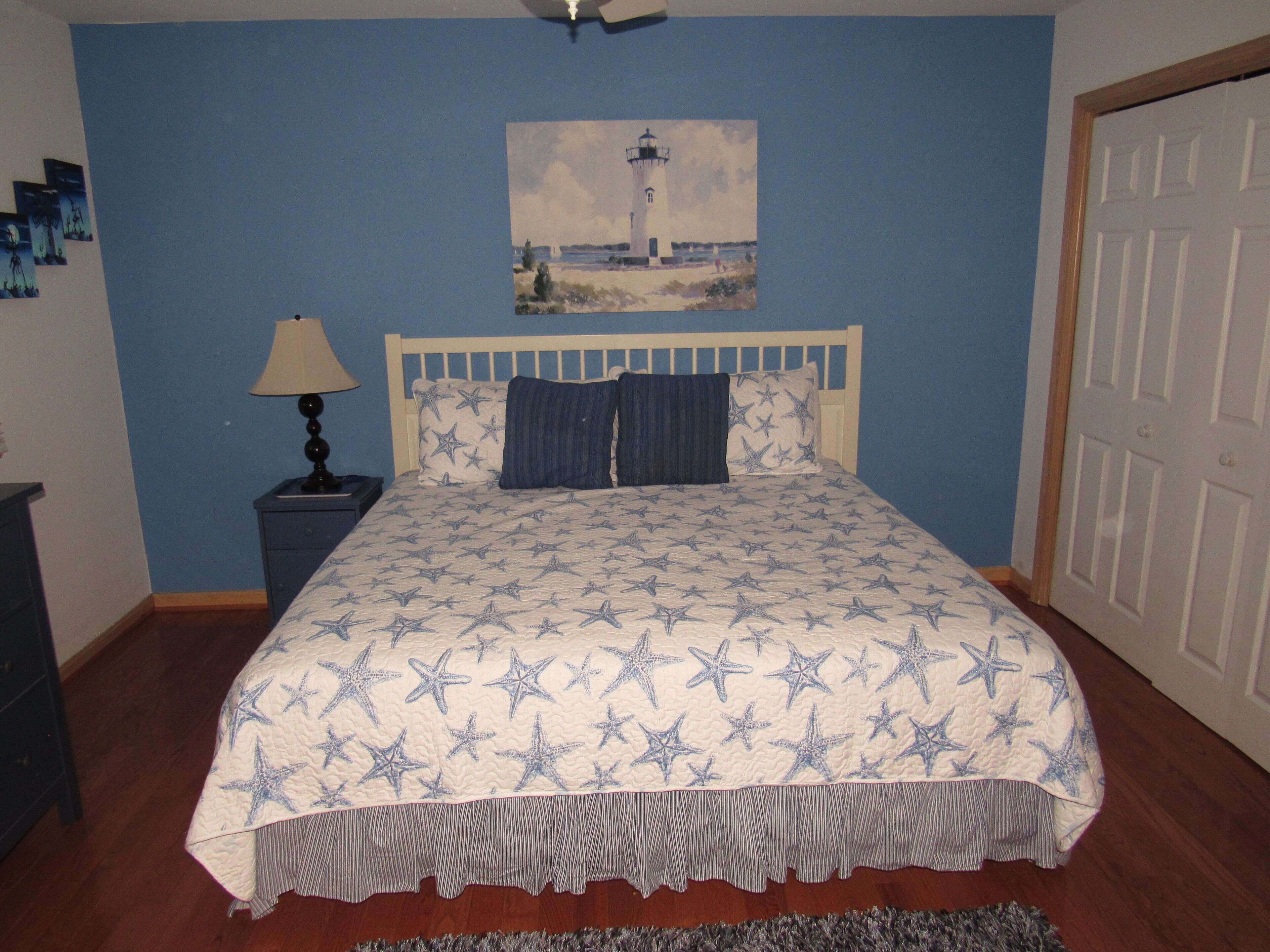 Un dormitorio con una cama, una mesita de noche, una lámpara, un cuadro y una puerta.