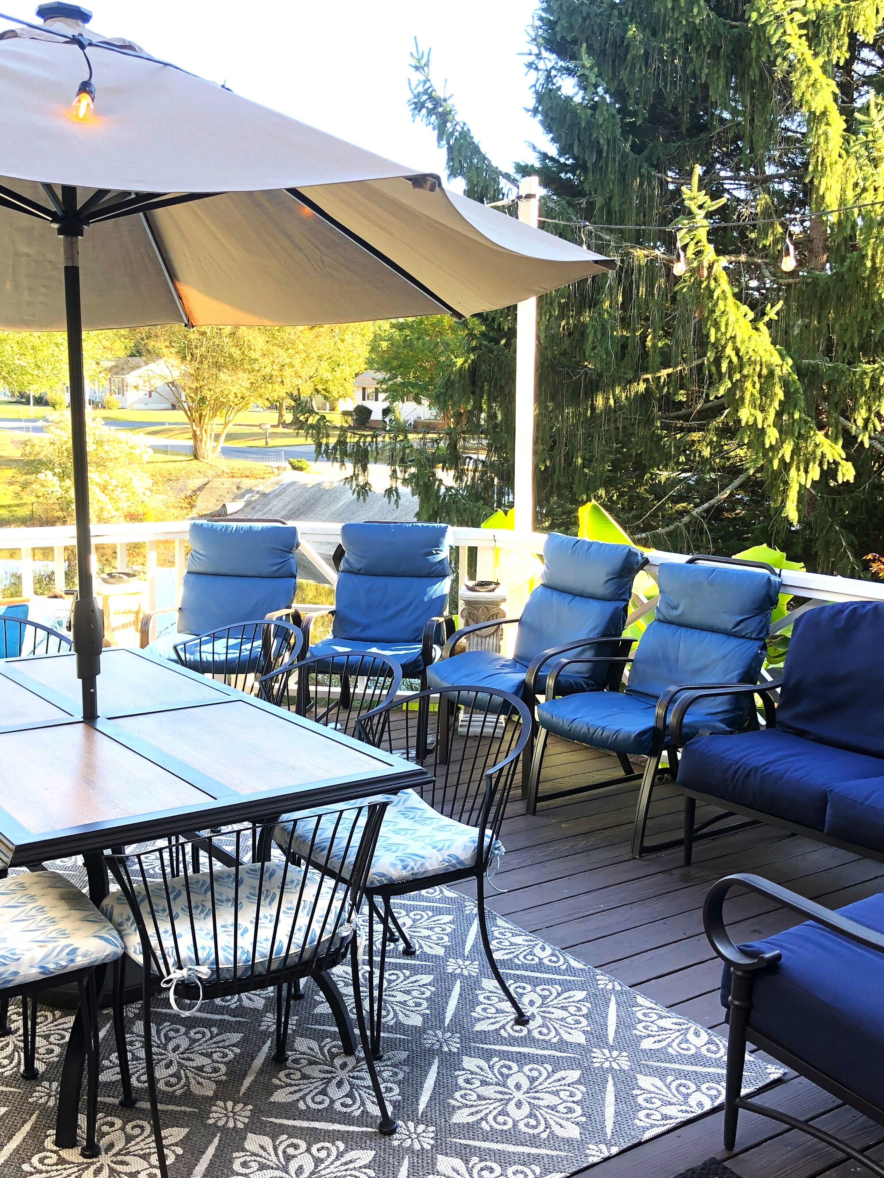 An outdoor patio with a table and chairs, a large umbrella, and a view of a residential area with trees and houses.