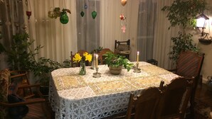 A dining area with a table set for two, surrounded by wooden chairs. There are potted plants on the table and hanging decorations.