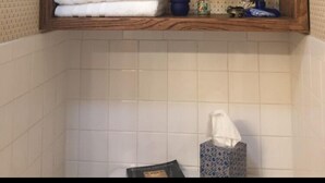 A bathroom with a wooden shelf holding towels, a decorative item, and a small blue container.