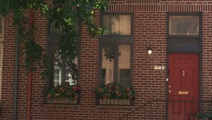 A brick building with a red door, windows with flower boxes, and a visible staircase.
