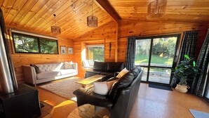 A cozy cabin interior with a fireplace, two sofas, a coffee table, and large windows offering a view of the outdoors. - Lake views, boating, skiing and hot pools (Omori)